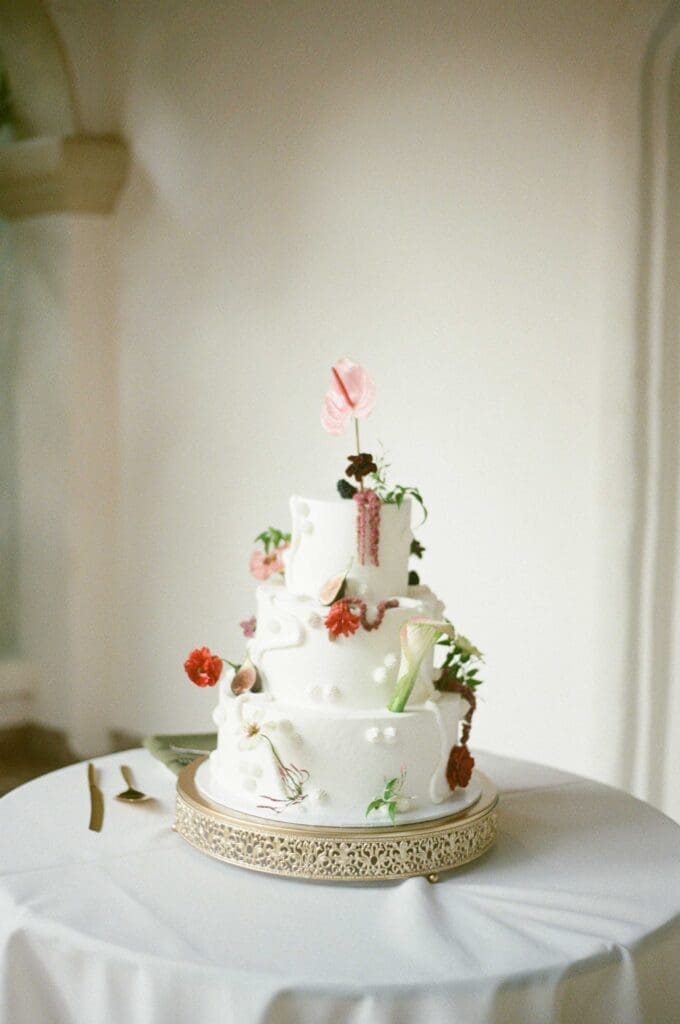 Film wedding photography detail shot of a three-tier cake decorated with anthurium and ranunculus florals.