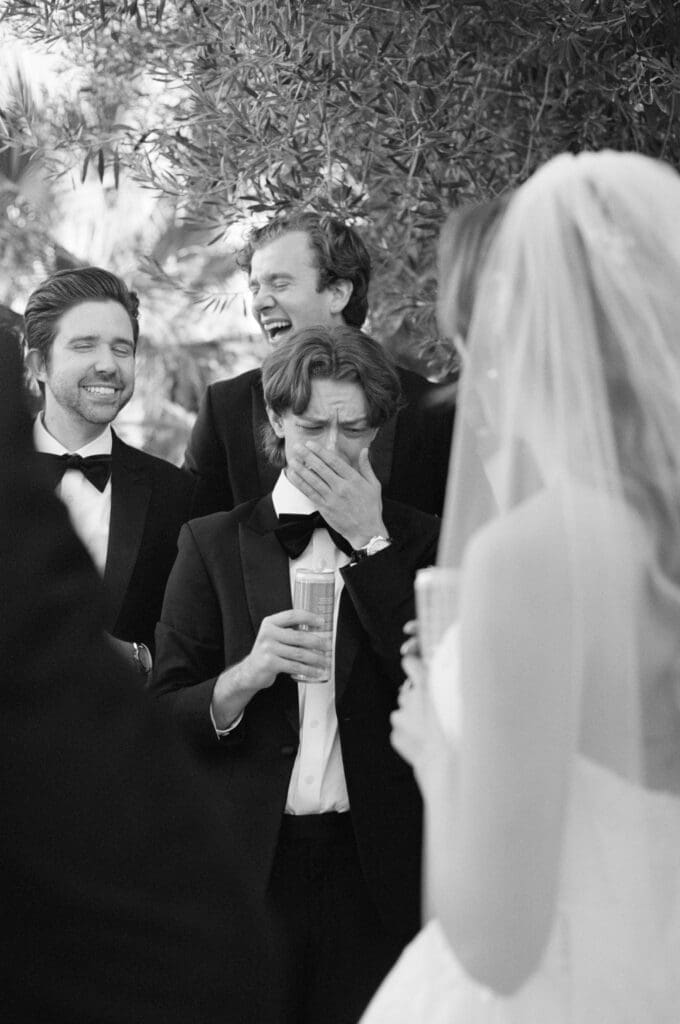 Black and white candid of groomsmen emotional with the bride, holding champagne.