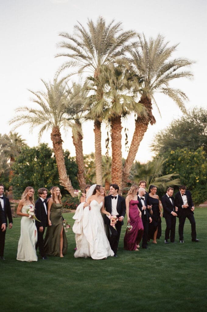 Full wedding party posing together on the lawn under tall palms at Bougainvillea Estate.