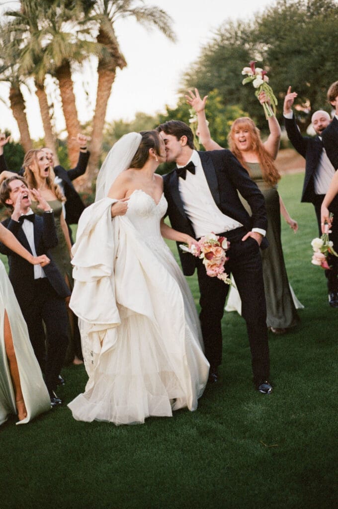 Wedding party cheering and celebrating around the newlyweds on the lawn at Bougainvillea Estate, a fun, lively moment.