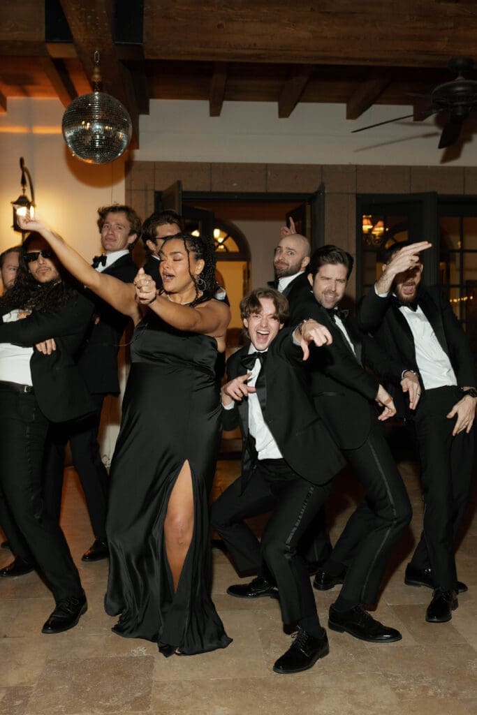Groom's party dancing with high energy under a disco ball, laughing and pointing toward the camera