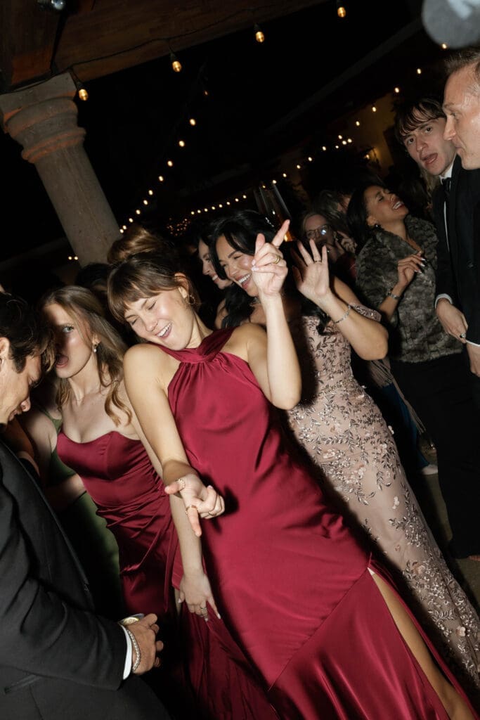 Guests in red and metallic gowns dancing with high energy on the dance floor.