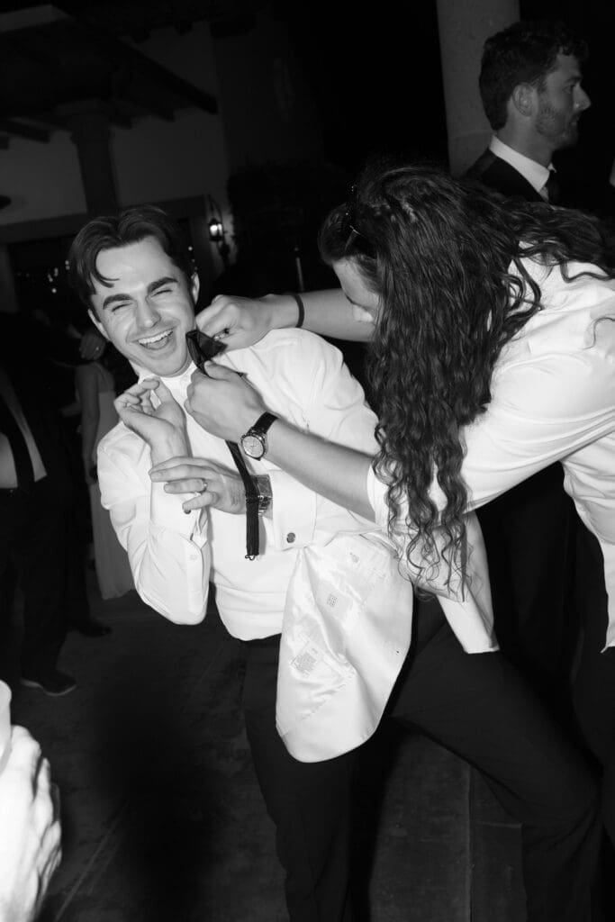 Black and white candid of the groom laughing and dancing with a guest.