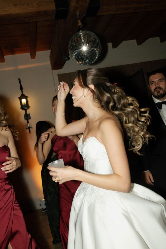 Bride dancing joyfully under a disco ball, surrounded by bridesmaids in red.