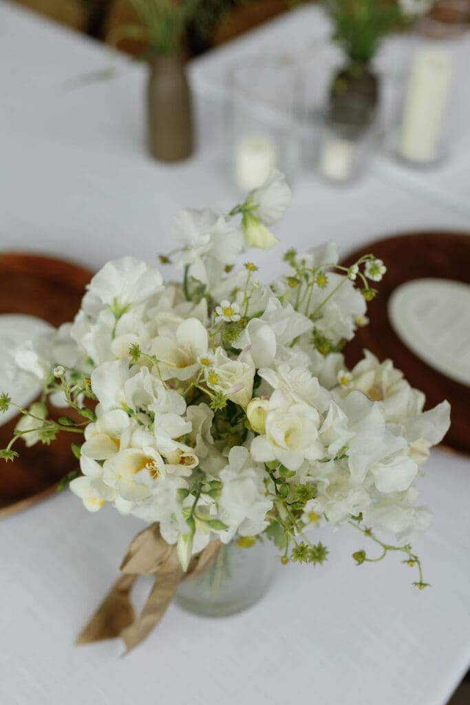 White floral centerpiece detail with candlelight on the reception table.