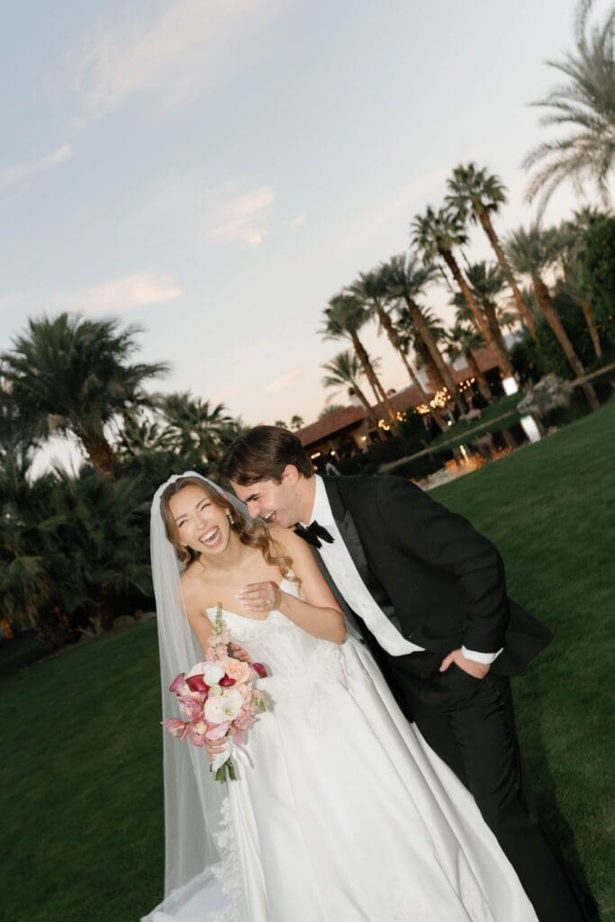 Bride and groom laughing together at dusk, a fun, lively moment on the lawn.