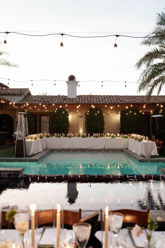 Candlelit dinner tables set poolside at Bougainvillea Estate, string lights strung overhead at sunset.