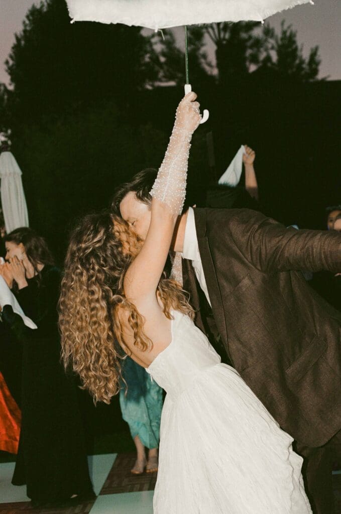 Bride and groom dancing under an umbrella at night, surrounded by guests during the reception.