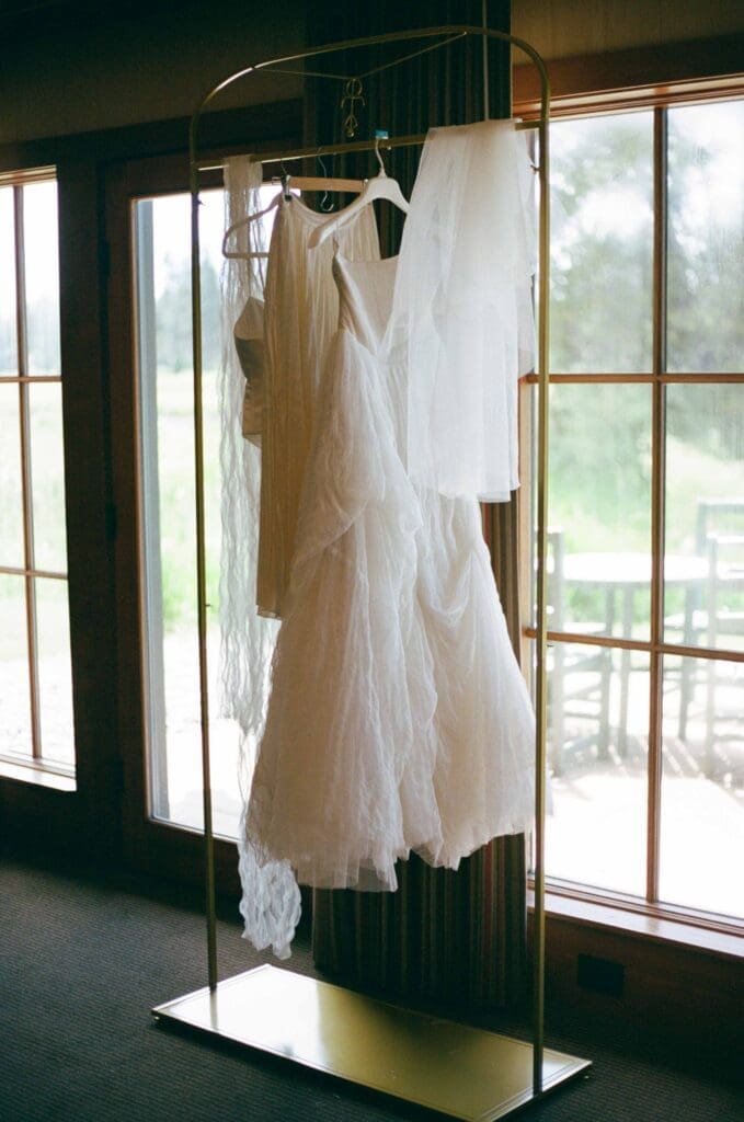 Film wedding photography of dresses hanging on a garment rack in soft window light.