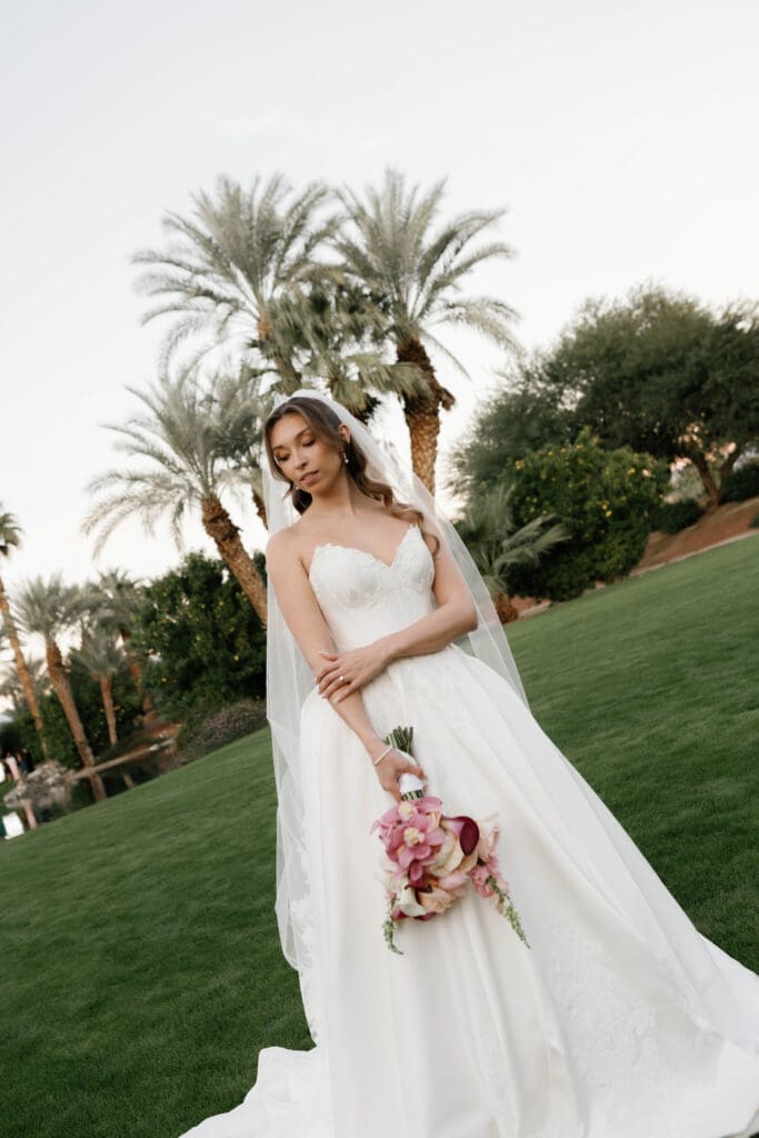 Bride standing on the lawn holding her bouquet, tall palm trees behind her