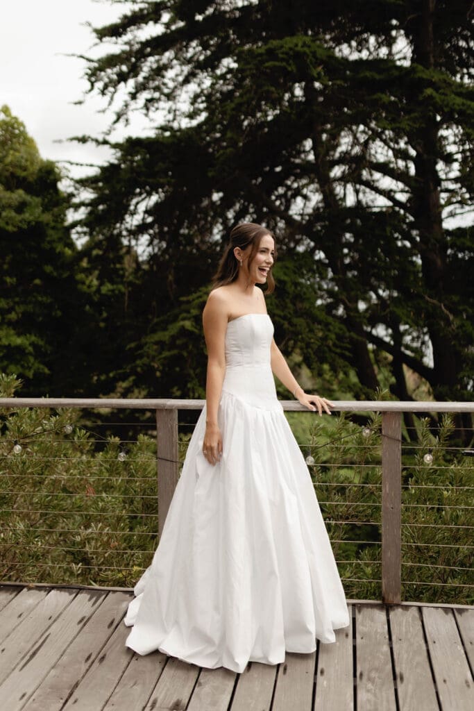 Bride laughing on the wooden deck, tall trees framing the background
