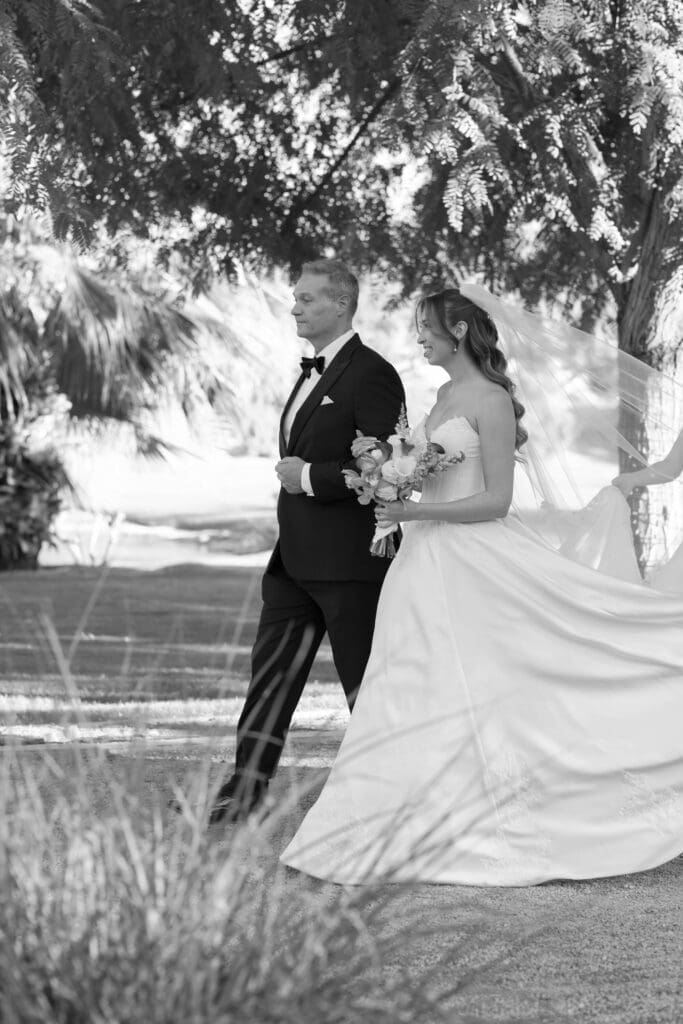 Black and white portrait of the bride and groom walking together outdoors, her bouquet in hand.