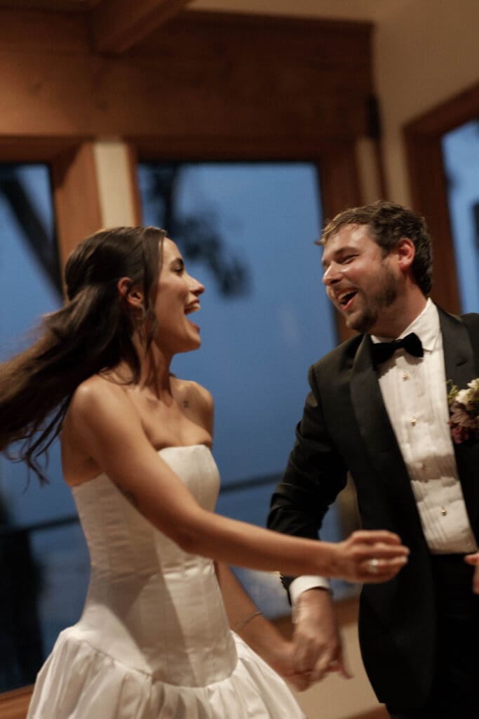 Bride and groom laughing while dancing together indoors during the reception.