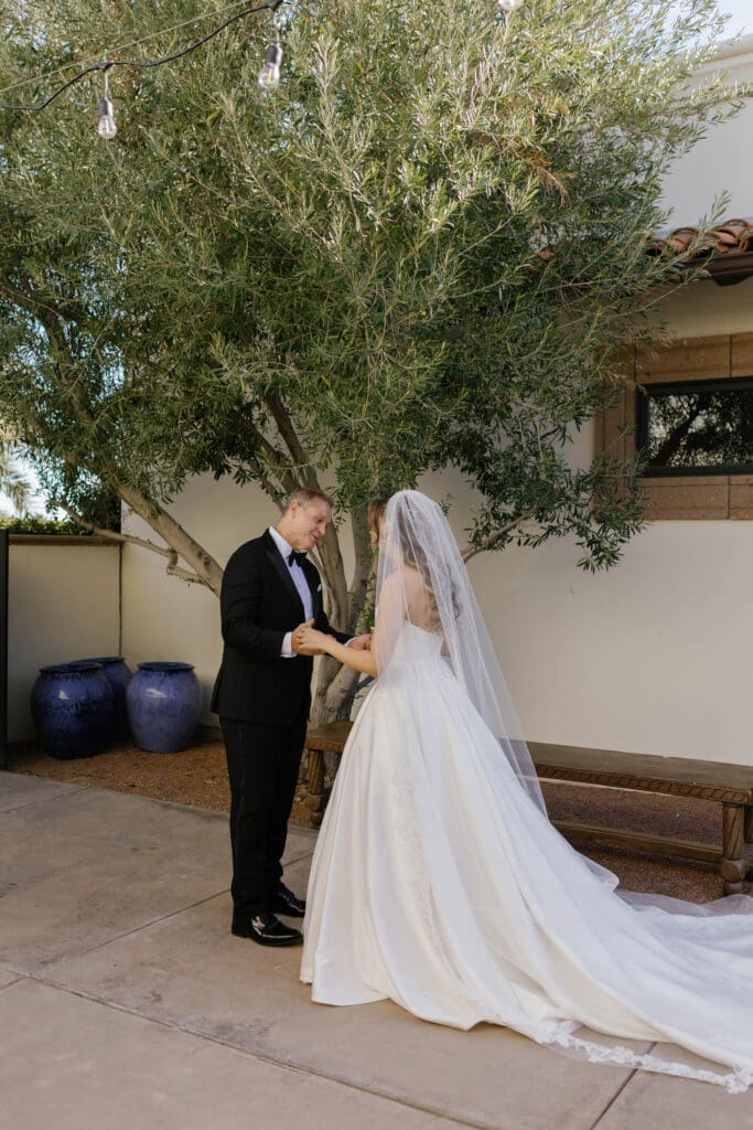 Bride and groom holding hands during their first look beneath an olive tree.