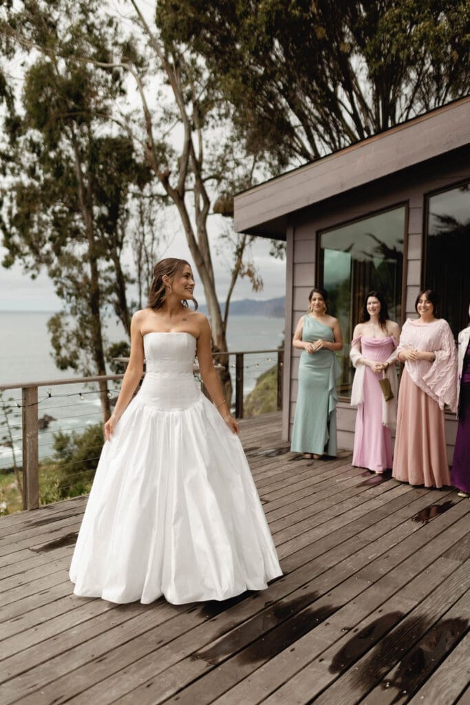 Bride laughing with bridesmaids in mismatched pastel dresses on the wooden deck."