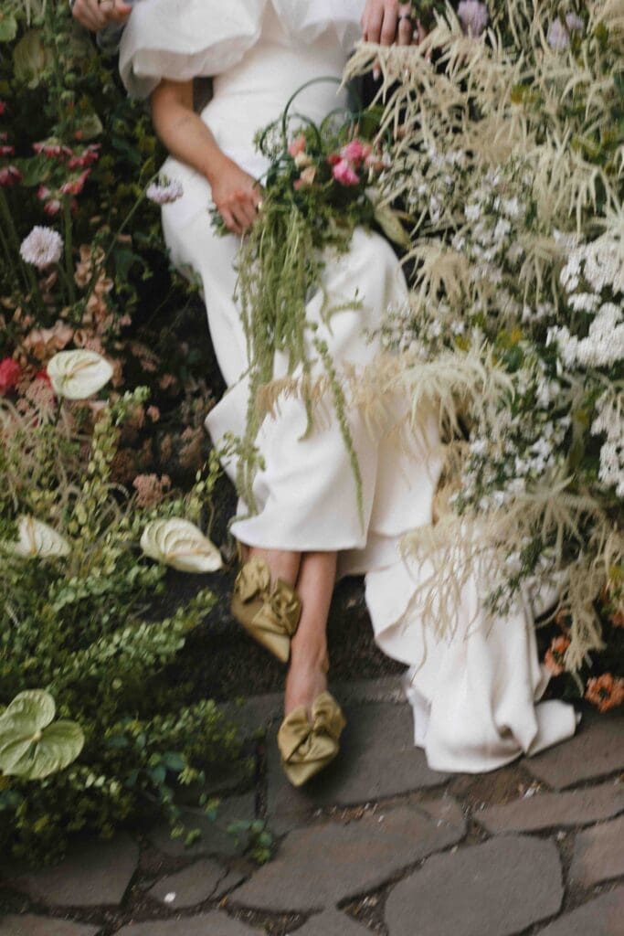 Digital wedding photography capturing a bride's gold shoes and flowing dress against a lush greenery-lined stone staircase.