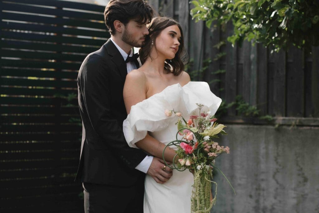 Digital wedding photography portrait of a bride and groom close together, her ruffled dress and bouquet in soft focus.