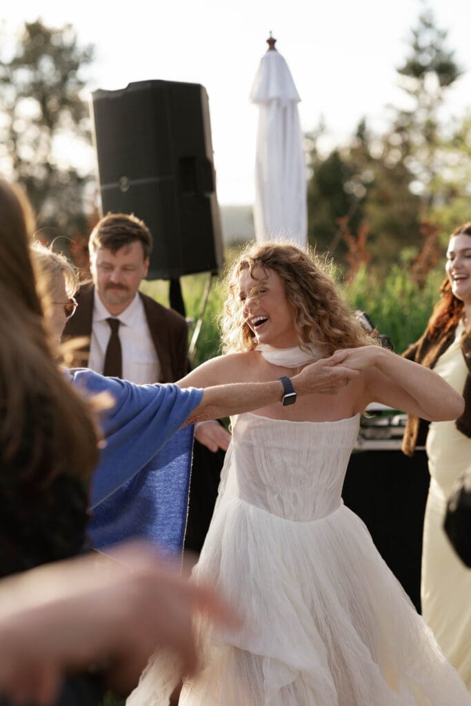 Bride dancing outdoors with guests near a speaker and white tent during the reception