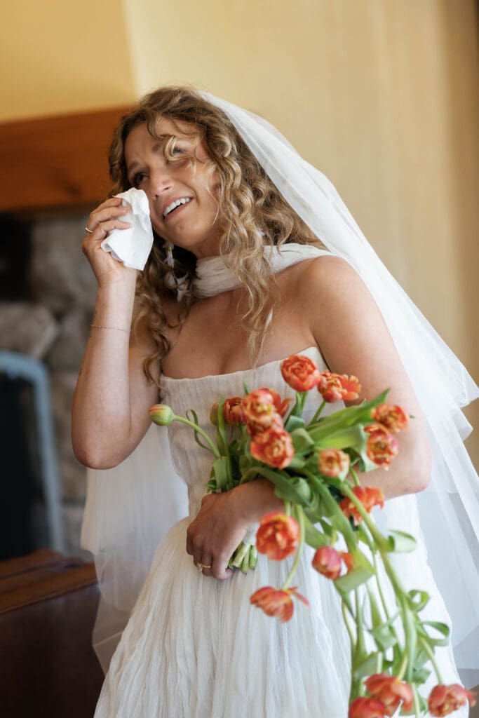Emotional moment of the bride wiping happy tears while holding her orange tulip bouquet, Sunriver Resort wedding, Central Oregon.