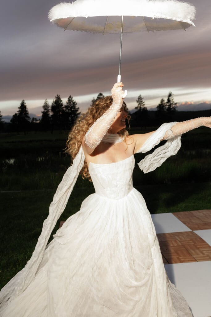 Bride twirling with a feathered white umbrella at dusk during her New Orleans inspired second line dance.
