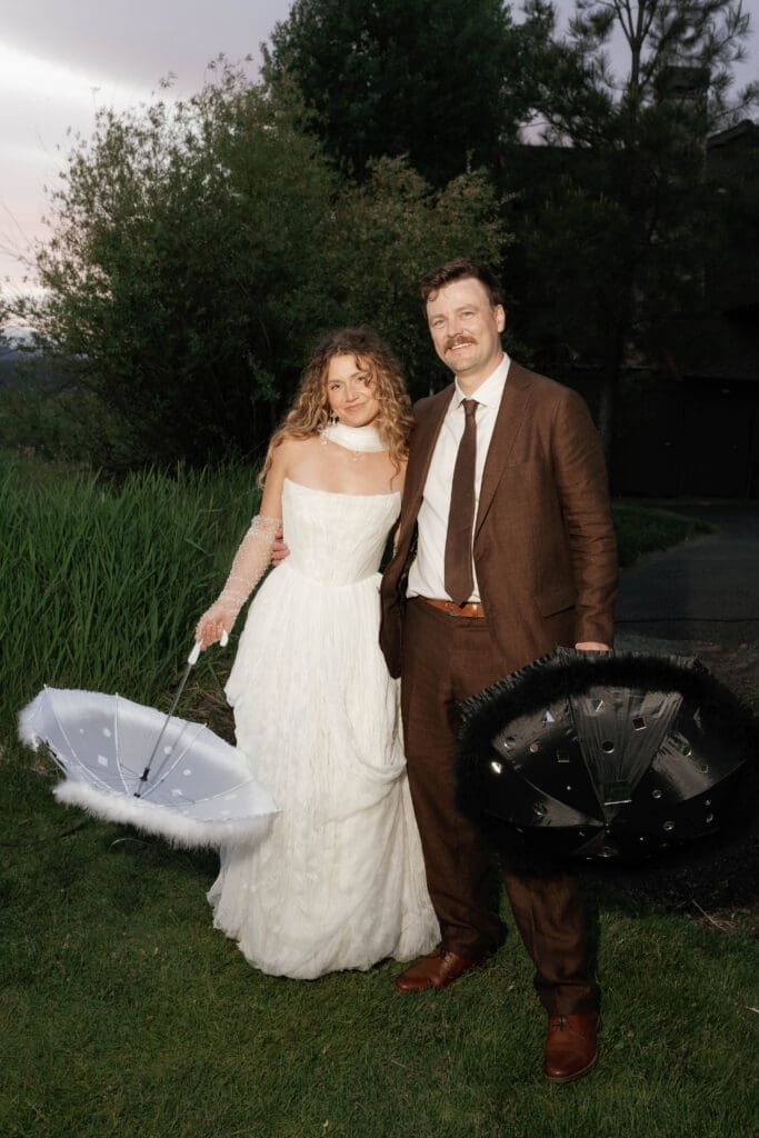 Bride and groom posing on the lawn with a polka-dot umbrella and decorative fan resting at their feet.