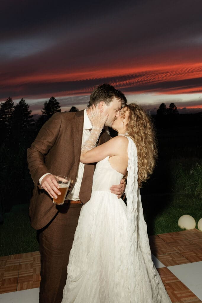 Bride and groom kissing on the dance floor under a vivid sunset sky, Sunriver Resort wedding, Central Oregon.