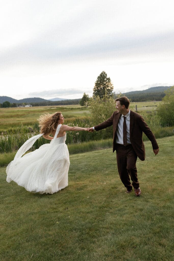 Bride and groom running and laughing while holding hands in an open field