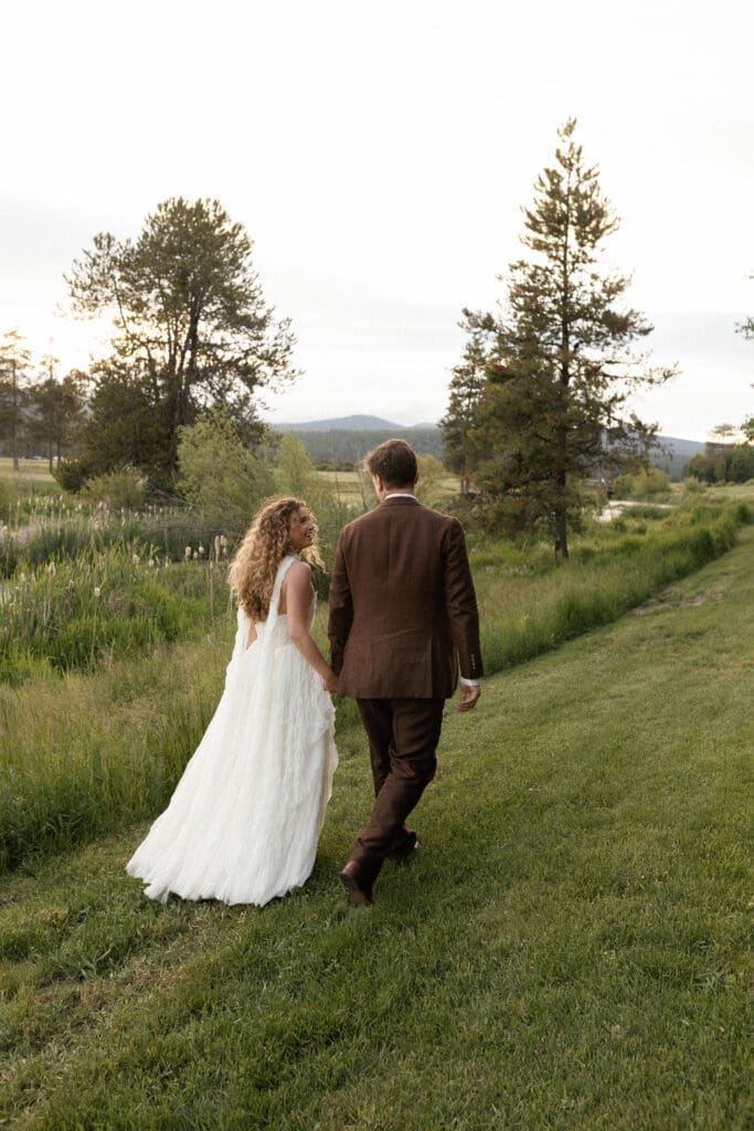 Bride and groom walking away hand-in-hand through the meadow