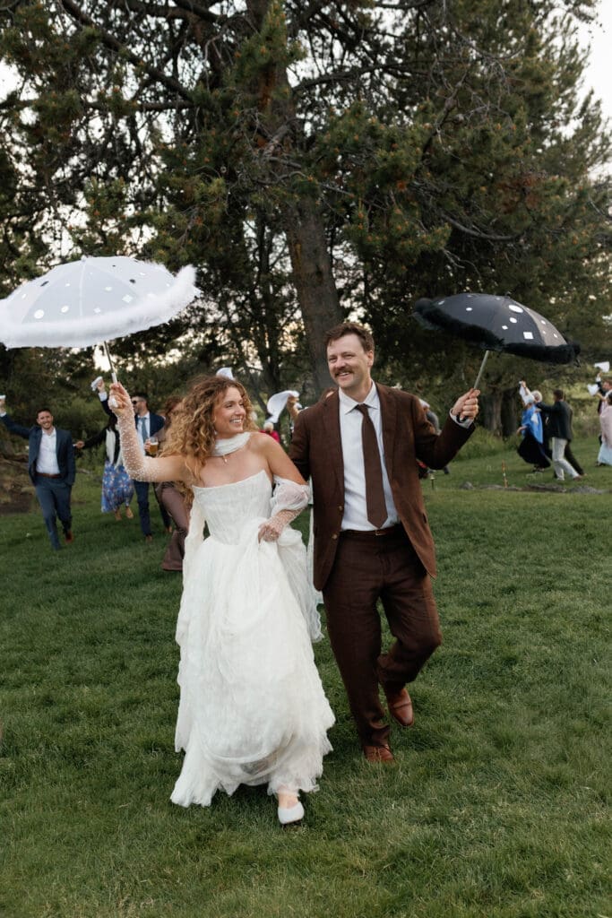 Bride and groom leading guests with polka-dot umbrellas across the lawn during their New Orleans inspired second line dance.