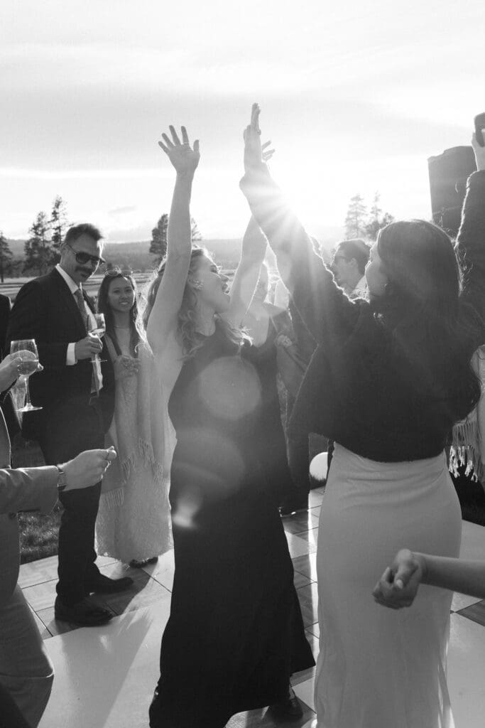 Black and white candid of wedding guests laughing and raising their arms on the dance floor.