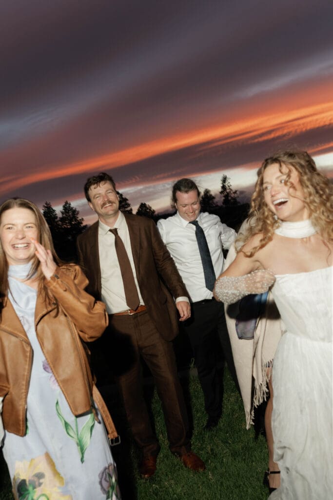 Bride and wedding guests laughing together at sunset, Sunriver Resort wedding, Central Oregon.
