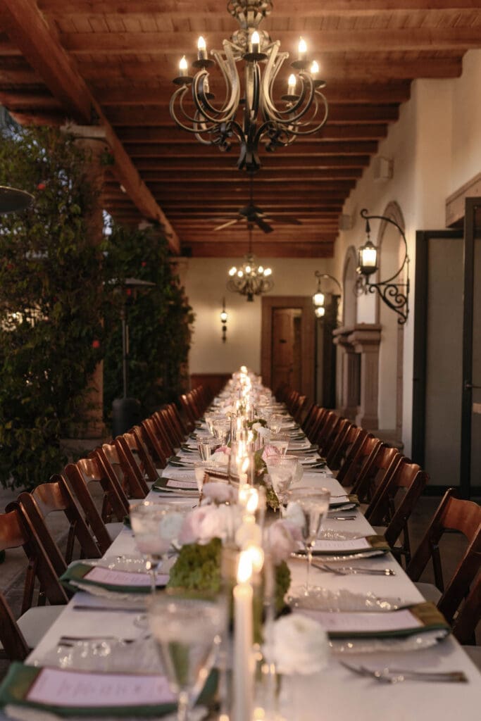 Long candlelit dinner table beneath Bougainvillea Estate's wood-beamed walkway and wrought iron chandelier.