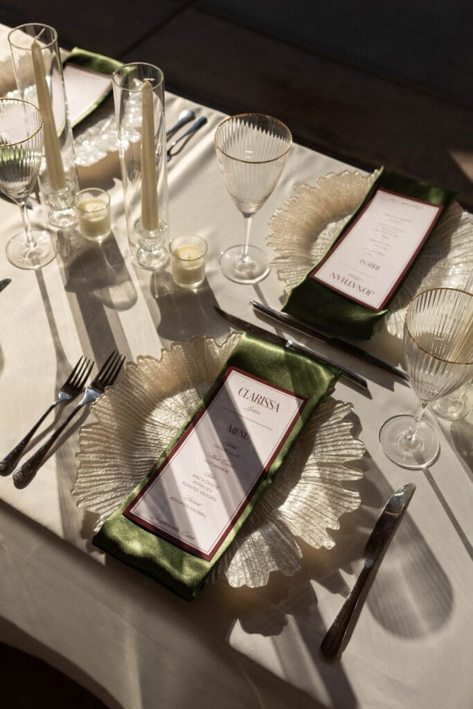 Reception place setting detail with a green menu card, silver charger plate, and candlelight.