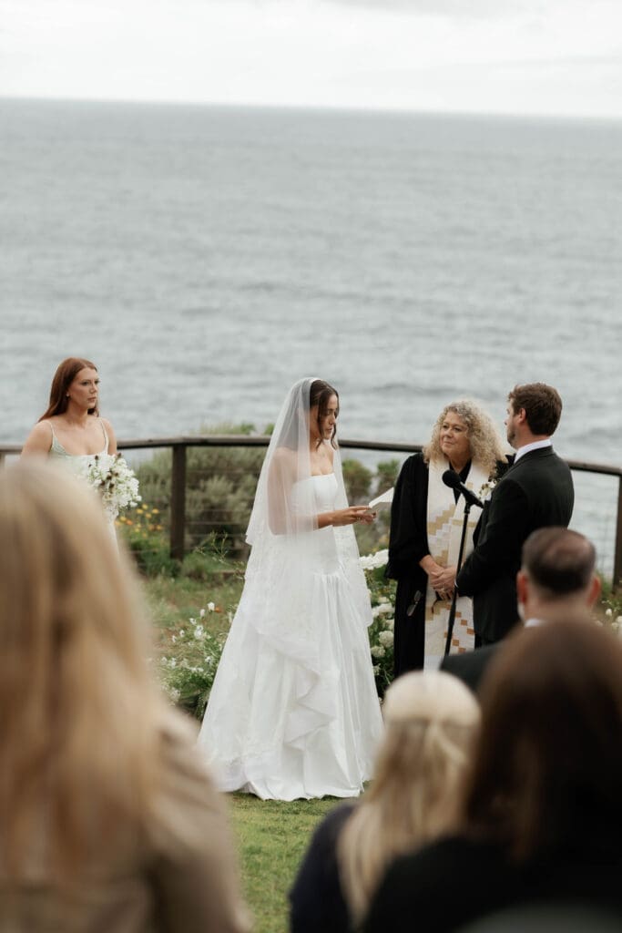 Bride and groom exchanging vows at their Wind and Sea Estate wedding ceremony, the Pacific Ocean stretching out behind them.