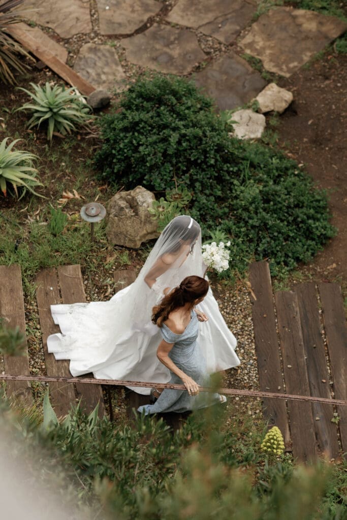 Aerial view of the bride and a bridesmaid descending a wooden stairway through the garden.