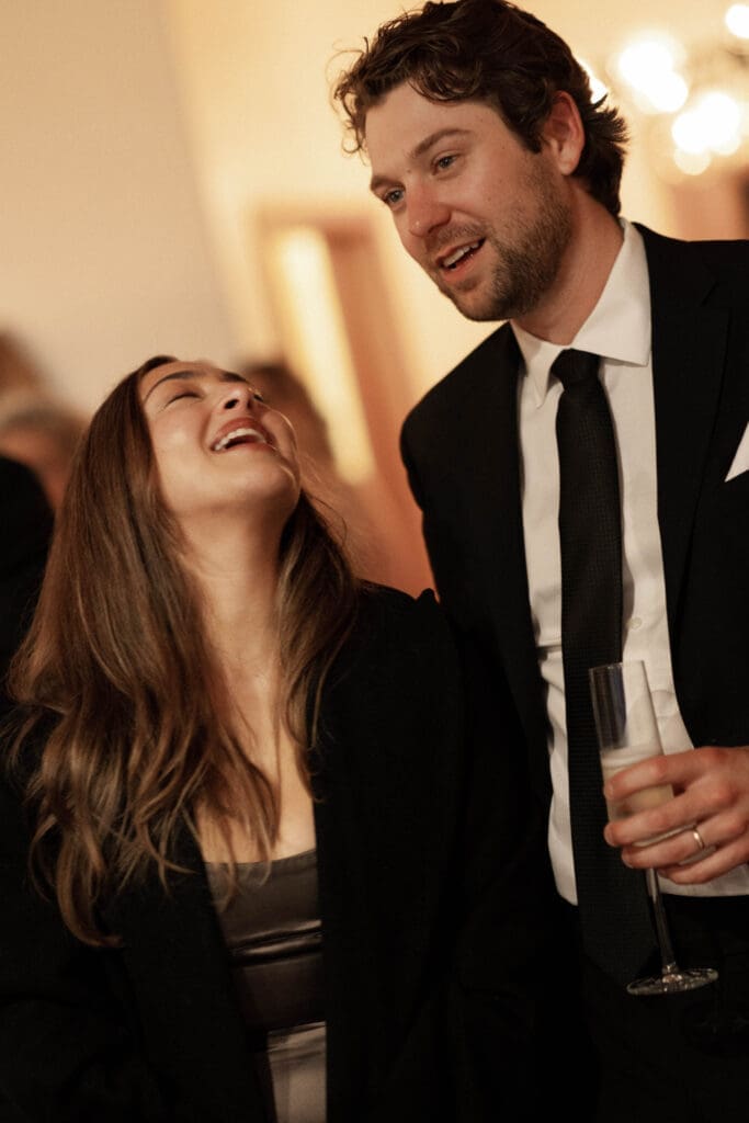 Guests laughing together at the reception under warm indoor lighting
