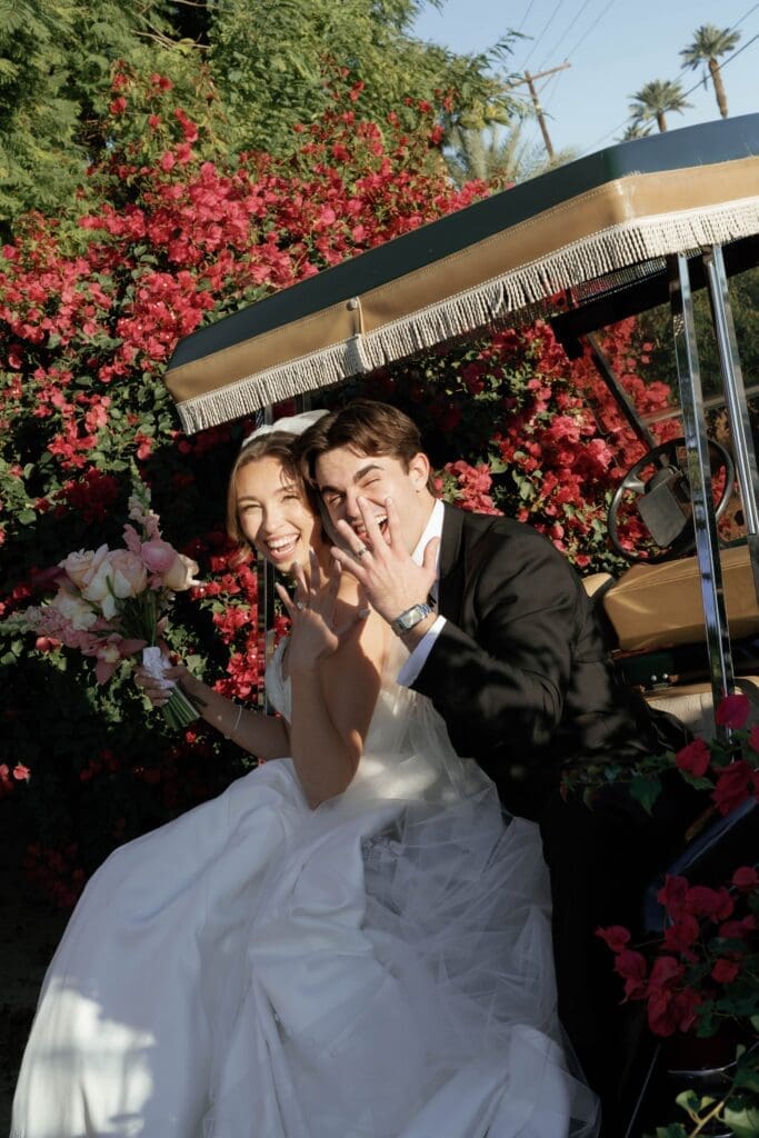 Bride and groom sharing a lively, fun moment beside a golf cart framed by real bougainvillea blooms.