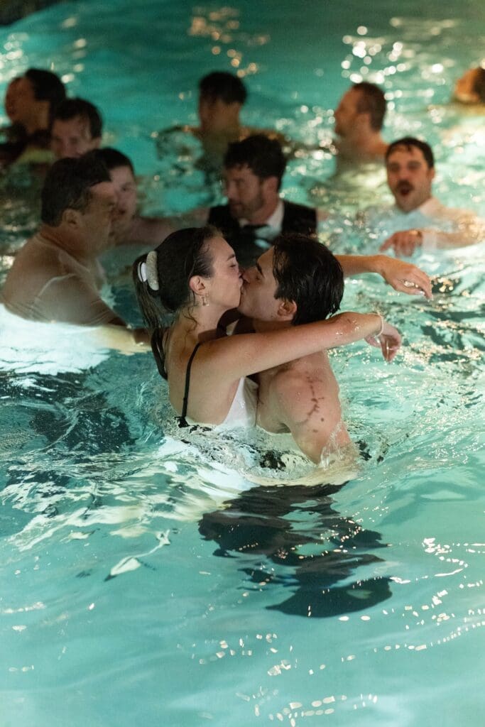 Bride and groom kissing in the pool surrounded by guests, a fun, unfiltered moment at the end of the night.