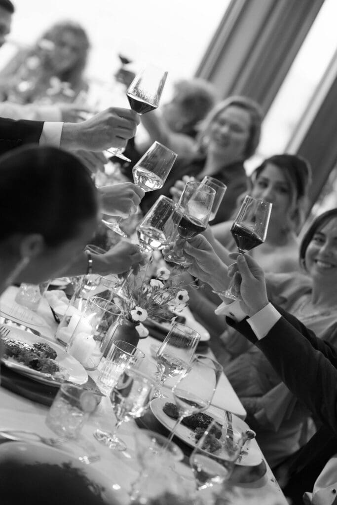 Black and white photo of guests raising their wine glasses in a toast.